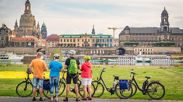 Gruppe von Radfahrenden am Dresdner Elbufer, im HIntergrund die Silhouette von Dresden - © The Photographer – stock.adobe.com